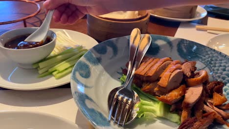 Delicious-Peking-duck-dish-with-cucumbers,-onions,-steamed-pancakes-and-hoisin-sauce,-picking-up-hoisin-sauce-with-a-spoon,-traditional-Asian-food-at-a-restaurant,-4K-shot