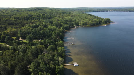 High-angle-panoramic-aerial-view-of-private-docks-reaching-to-deep-blue-water-from-forested-hills-in-maple-lake-ontario