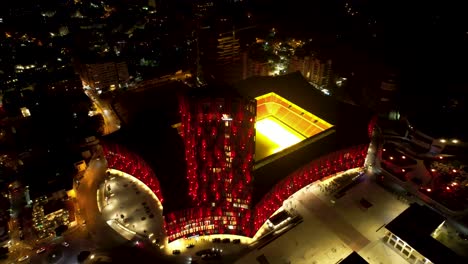 Tirana's-Vibrant-Nightscape:-Aerial-Drone-View-of-the-Colorful-Stadium-Facade-Illuminated-in-the-Capital-City's-Nighttime-Glory