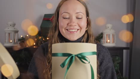 European-woman-looks-inside-round-gift-box-at-joyful-holiday-christmas-season,-yellow-light-bokeh-flutters