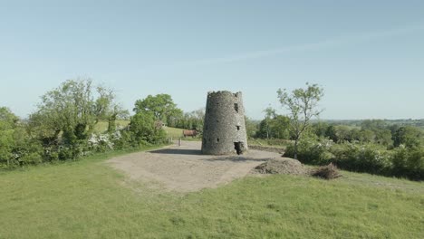 Ruined-Medieval-Celtic-Round-Tower-In-Green-Field,-Midlands,-Ireland---aerial-drone-shot