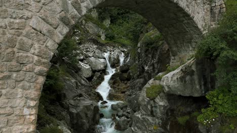 Fliegen-Unter-Dem-Bogen-Einer-Backsteinbrücke,-Während-Der-Flusswasserstrom-In-Der-Sommersaison-Im-Furka-Pass-Tal-Der-Schweiz-Fließt