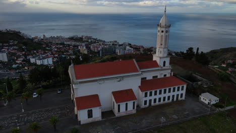 Luftaufnahme-Der-Sao-Martinho-Kirche-In-Funchal,-Madeira:-Umlaufbahn-über-Der-Wunderschönen-Kirche-Bei-Sonnenuntergang-Und-Blick-Auf-Die-Stadt-Und-Das-Meer