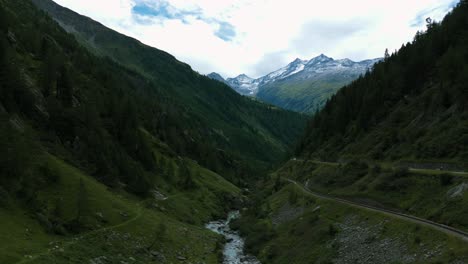 Aerial-view-of-Furka-Pass-valley-and-river-stream-flowing-in-Switzerland-with-mountain-peaks-in-background