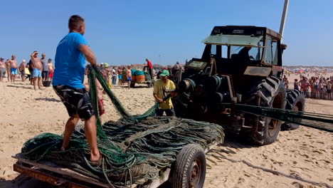 Tractor-pulling-trawl-fishing-nets-or-Xávega-gear-on-the-beach-during-the-bathing-season,-fishermen-rolling-up-the-nets-on-top-of-the-tractor