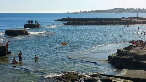 Natural-pools-of-sea-water-with-young-people-in-the-background-jumping-from-the-rocks-into-the-blue-water