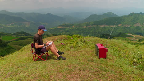 Male-sitting-in-outdoors-hilltop-nature-watching-old-television-and-taking-notes