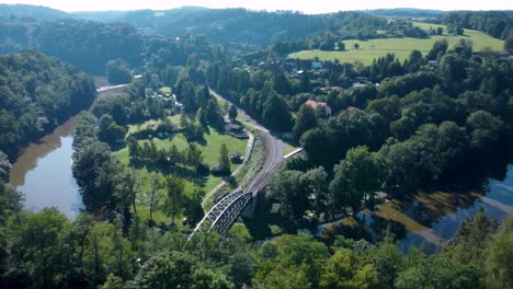 Luftaufnahme-Einer-Eisenbahnbrücke-über-Einem-Fluss-Mit-Sonnenreflexionen-Und-Wäldern-In-Der-Umgebung
