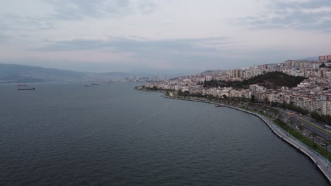 Aerial-drone-video-of-goztepe-izmir-with-mountain,-eagean-sea-in-the-background-at-sunset-with-traffic-flow