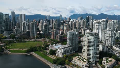 Rise-Aerial-shot-of-Vancouver-City-Downtown-with-skyscraper-buildings-and-mountains-in-background---Falls-Creek-River-in-foreground---Beautiful-panorama-city-view-in-Canada