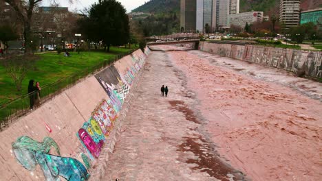 Drone-tracking-shot-of-a-lovely-couple-walking-alone-beside-the-Mapocho-River-in-Santiago-Chile