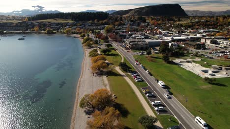 Lakeside-of-lake-Wanaka-township,-beach-lined-by-colorful-trees,-skate-park-and-playground