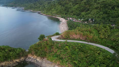 Stunning-aerial-flyover-shot-of-motorcycle-driving-on-cliffside-road-in-lush-island-of-Catanduanes,-Philippines