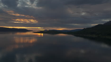 Aerial-over-serene-Norwegian-fjord,-scenic-golden-sunset-illuminates-cloudy-sky