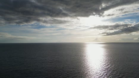 Ocean-aerial-drone-high-view,-sun-reflection-at-golden-hour-hidden-behind-clouds