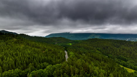 Aerial-hyper-lapse-over-highway-cutting-through-verdant-forest,-moody-clouds