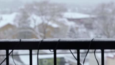 Slow-motion-shot-close-up-of-snowflakes-falling-during-a-old-winter-snowstorm-with-an-apartment-balcony-railing-and-other-buildings-and-trees-out-of-focus-in-the-background-in-Midvale-Utah-in-December