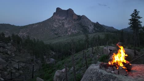 Male-camper-stokes-campfire-atop-boulder-in-San-Isabel-National-Forest,-drone