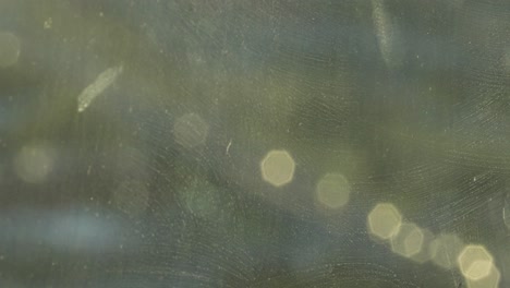 Artistic-six-sided-bokeh-of-car-lights-gleam-out-of-focus-on-a-dirty-glass-window-creating-a-golden-green-abstract-experience