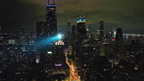 Aerial-view-backwards-away-from-the-night-lit-Chicago-skyline---pull-back,-drone-shot
