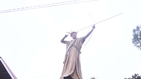 Daytime-revolving-shot-around-the-sculpture-of-a-Shipibo-local-archer-aiming-in-Oxapampa,-Peru