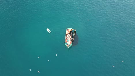 Aerial-view-of-a-fishing-trawler-towing-its-net,-filling-sardines-and-seagulls-hovering-around