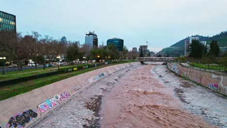 Drone-dolly-in-shot-of-the-Mapocho-river-water-flowing-through-Santiago-Chile-with-great-force-on-a-cloudy-sunset