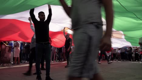 Während-Einer-Protestkundgebung-Auf-Dem-Trafalgar-Square-Anlässlich-Des-Einjährigen-Todestages-Von-Mahsa-Amini-Schieben-Und-Wehen-Demonstranten-Eine-Riesige-Iranische-Flagge-Von-Unten