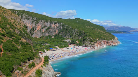Aerial-drone-backward-moving-shot-over-tourists-thronging-on-secluded-Gjipe-Beach-in-Dhermi,-Albania-on-a-sunny-day
