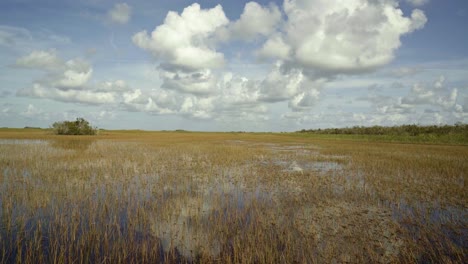 Nach-Unten-Geneigte-Aufnahme-Der-Atemberaubenden-Florida-Everglades-In-Der-Nähe-Von-Miami-In-Der-Mitte-Auf-Einem-Luftkissenboot,-Wobei-Das-Ruhige-Sumpfwasser-Den-Himmel-Reflektiert-Und-An-Einem-Sonnigen-Tag-Eine-Fata-Morgana-Inmitten-Von-Hohem-Gras-Erzeugt