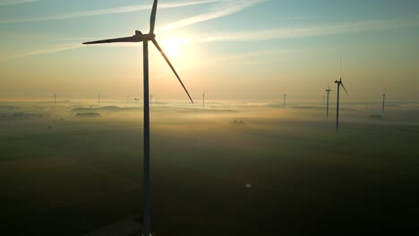 A-beautiful-shot-of-a-picturesque-landscape-shrouded-in-mist-at-dawn,-with-the-spinning-propellers-of-wind-turbines-towering-above