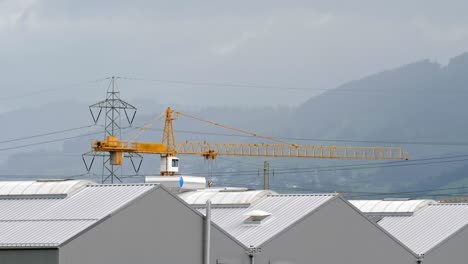 Yellow-Construction-Crane-With-Electricity-Pylon-In-Background-At-Warehouse-Industrial-Site-On-Rainy-Overcast-Day