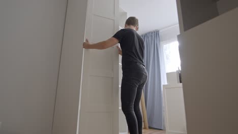 Low-angle-upwards-view-of-man-assembling-and-rotating-tall-shelf-door-up-in-clean-white-room