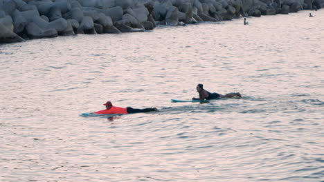 Surfer-Instructor-Together-With-His-Student-Paddling-In-The-Water-While-Lying-On-Surfboard-In-Sokcho,-South-Korea