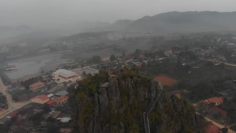 Flying-around-big-rock-at-Laos-small-town,-aerial