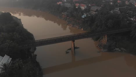 A-local-bridge-over-the-mekong-at-luang-prabang-Laos-during-rush-hour,-aerial