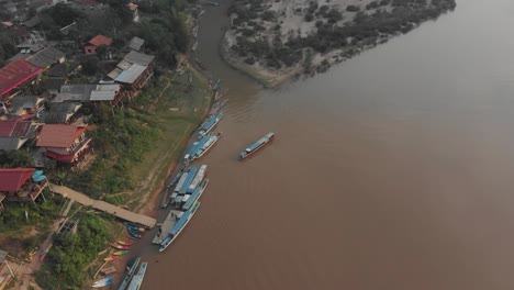 Top-down-view-of-Muang-Ngoy-with-boats-on-nam-ou-river-during-sunset,-aerial