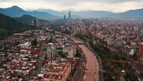 Drone-establishing-shot-of-Santiago-Chile-with-the-financial-center-and-the-snowy-Andes-mountain-range-in-the-background,-Costanera-tower