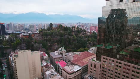 Flyover-in-downtown-Santiago-dolly-in-with-the-greenish-Santa-Lucia-hill-and-the-Andes-mountain-range-in-the-background,-Chile