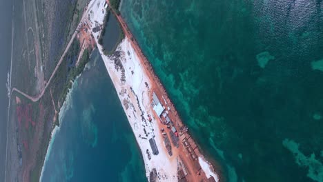 Vertical-high-angle-shot-of-large-construction-site-surrounded-by-clear-Caribbean-sea-in-summer---port-cabo-rojo-in-Pedernales