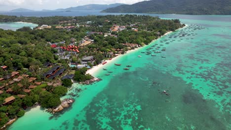 Koh-Lipe-Thailand-coastline-with-boats-docked-and-turquoise-water-with-coral-reefs--aerial-fly-in