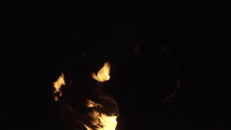 In-the-darkness-of-the-night,-the-silhouette-of-a-bearded-man's-head-is-visible-in-front-of-a-burning-fire