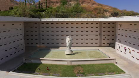 Reverse-pullback-close-up-aerial-shot-of-a-Catholic-angel-statue-in-front-of-a-stone-mausoleum-at-a-California-mortuary