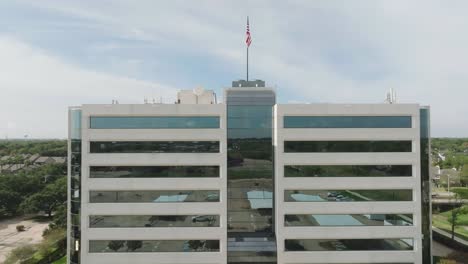 Eine-Luftaufnahme-Eines-Modernen-Mehrstöckigen-Bürogebäudes-Mit-Einer-Amerikanischen-Flagge-Auf-Dem-Dach,-Die-Sanft-Im-Wind-Weht,-In-Houston,-Texas
