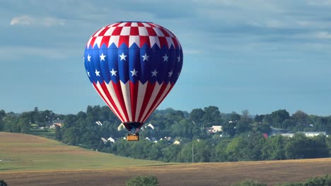 American-flag-hot-air-balloon-soars-above-rural-farmland-of-Lancaster-County,-Pennsylvania,-USA