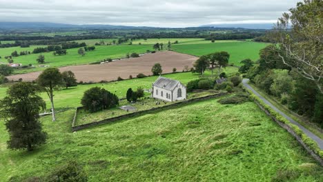 Vuelo-Aéreo-A-Una-Iglesia-Romántica-En-Fértiles-Y-Verdes-Tierras-De-Cultivo-De-Waterford,-Irlanda,-En-Una-Mañana-De-Septiembre