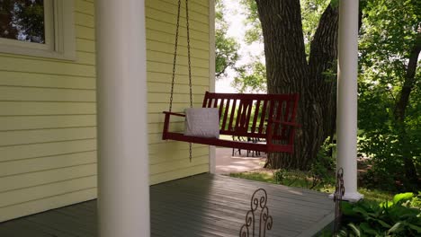 orbiting-shot-of-a-red-hanging-swing-on-the-front-deck-of-a-farmhouse