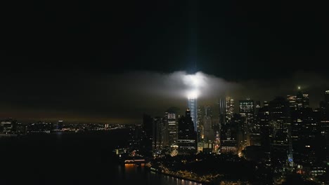 Eine-Luftaufnahme-Des-Freedom-Tower-In-New-York-City-Bei-Nacht,-Mit-Der-Hommage-In-Hellen-Doppelstrahlen-Beleuchtet