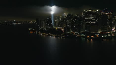 Eine-Luftaufnahme-Des-Freedom-Tower-In-New-York-City-Bei-Nacht,-Mit-Der-Hommage-In-Hellen-Doppelstrahlen-Beleuchtet