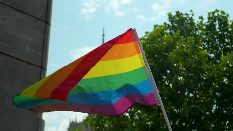 The-LGBT-flag-on-a-white-pole-flutters-in-the-wind,-with-a-section-of-the-Palace-of-Culture-in-the-background---Equality-March-in-Warsaw-in-June-2023